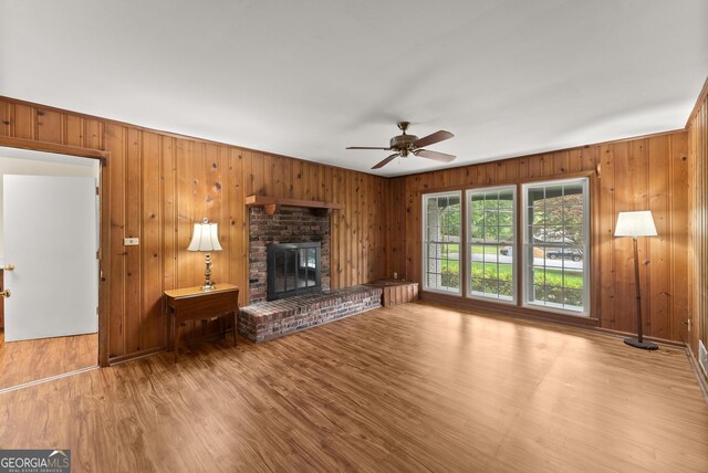 unfurnished living room featuring a fireplace, a ceiling fan, wood walls, and wood finished floors