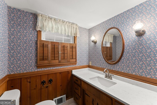 bathroom with visible vents, wainscoting, vanity, and wallpapered walls