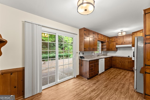 kitchen featuring freestanding refrigerator, white dishwasher, light wood-type flooring, under cabinet range hood, and a sink