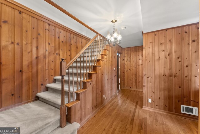 stairs featuring visible vents, wood walls, baseboards, a chandelier, and hardwood / wood-style flooring