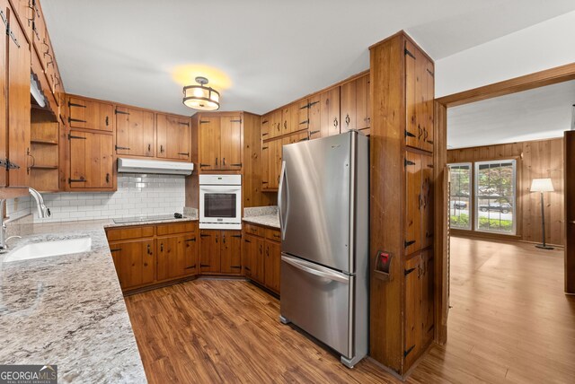 kitchen with brown cabinetry, white oven, a sink, freestanding refrigerator, and under cabinet range hood