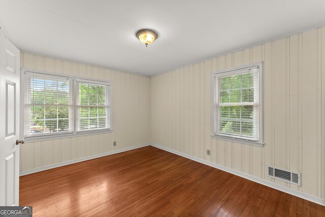 spare room featuring visible vents, baseboards, a wealth of natural light, and hardwood / wood-style flooring