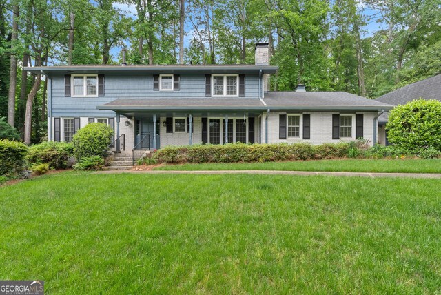 traditional-style home with covered porch, a chimney, brick siding, and a front yard