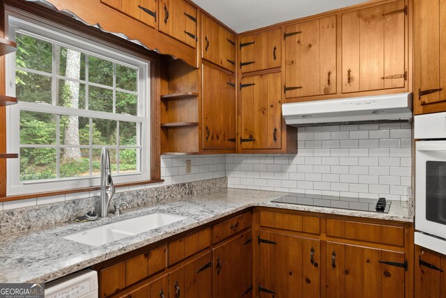 kitchen with under cabinet range hood, black electric cooktop, decorative backsplash, and a sink