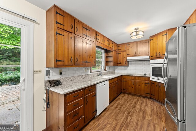 kitchen featuring a sink, brown cabinets, under cabinet range hood, and white appliances