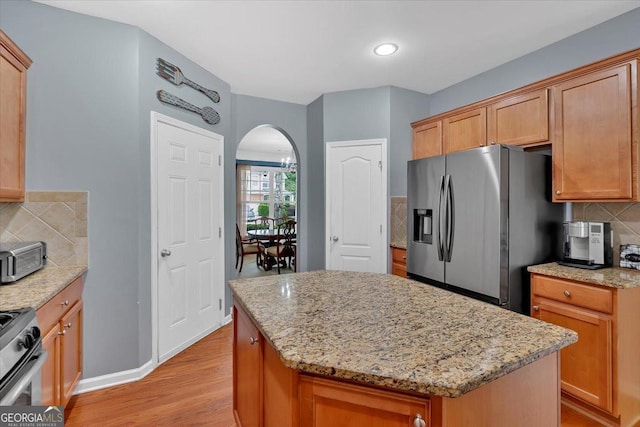 kitchen featuring stainless steel appliances, arched walkways, light stone countertops, and backsplash