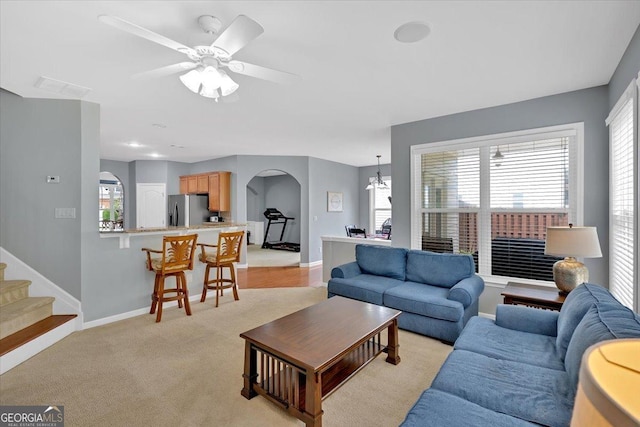 living room featuring arched walkways, baseboards, a ceiling fan, and stairway