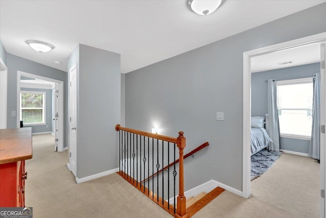 hall with an upstairs landing, light colored carpet, and baseboards