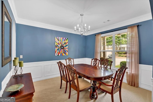 dining area featuring a chandelier, wainscoting, light colored carpet, ornamental molding, and a decorative wall
