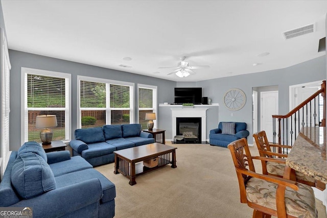 living room with ceiling fan, light carpet, a glass covered fireplace, and stairs