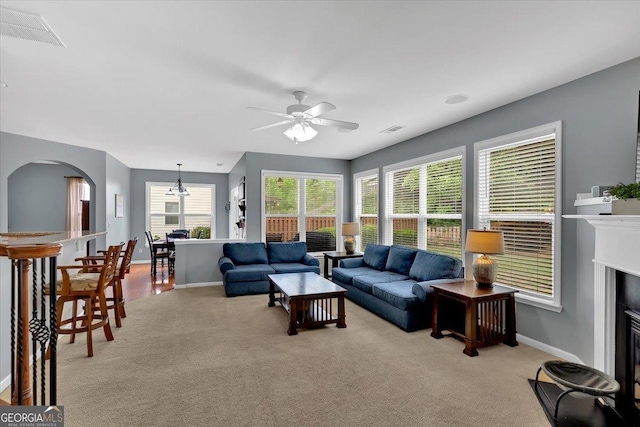 living area featuring ceiling fan, light colored carpet, baseboards, and arched walkways