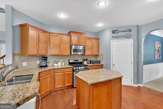 kitchen with appliances with stainless steel finishes, a sink, arched walkways, light wood finished floors, and light stone countertops
