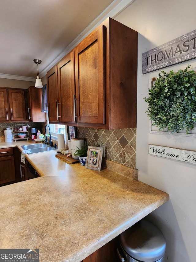 kitchen with hanging light fixtures, a sink, light countertops, tasteful backsplash, and ornamental molding