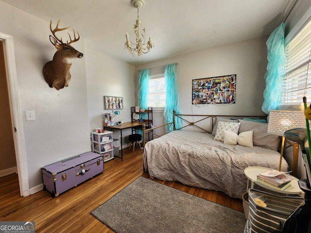 bedroom with baseboards, wood finished floors, and a notable chandelier