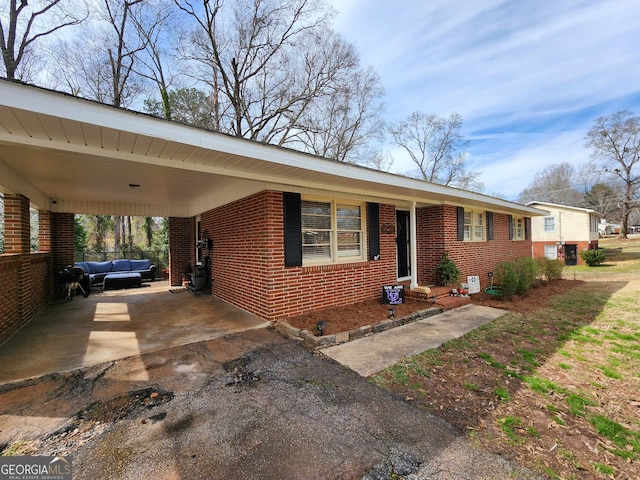 single story home featuring brick siding, an outdoor living space, driveway, and an attached carport