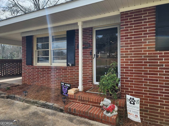 doorway to property featuring a porch and brick siding