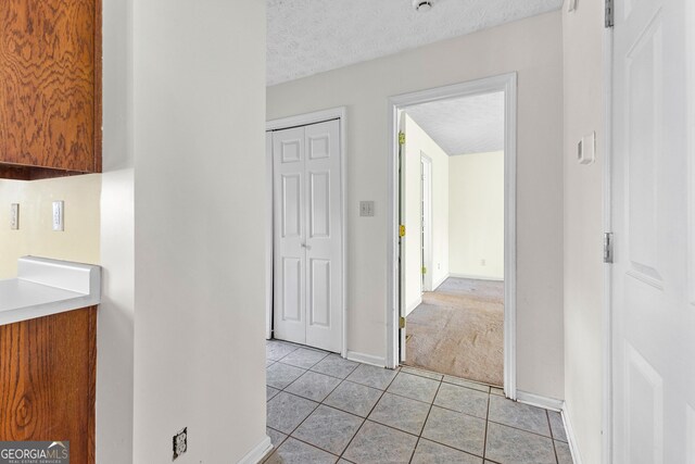 hallway with a textured ceiling, baseboards, light colored carpet, and light tile patterned floors