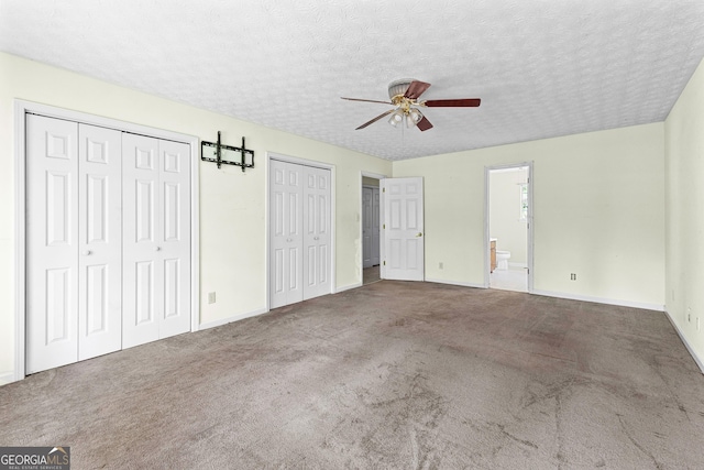 unfurnished bedroom featuring carpet floors, a textured ceiling, multiple closets, and baseboards
