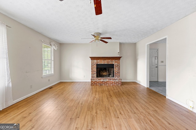 unfurnished living room with a fireplace, baseboards, ceiling fan, light wood-type flooring, and a textured ceiling