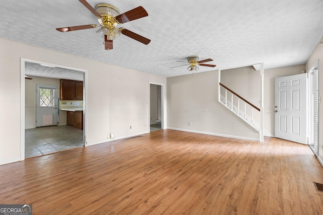 unfurnished living room featuring visible vents, stairway, a textured ceiling, a ceiling fan, and light wood finished floors