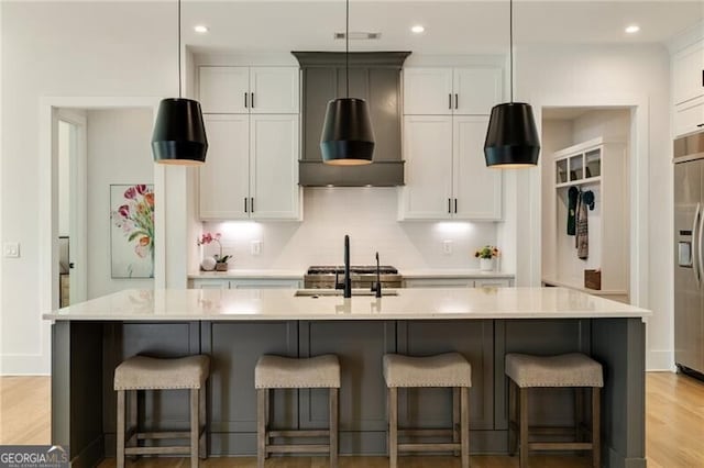 kitchen with light countertops, built in refrigerator, a center island with sink, and a breakfast bar