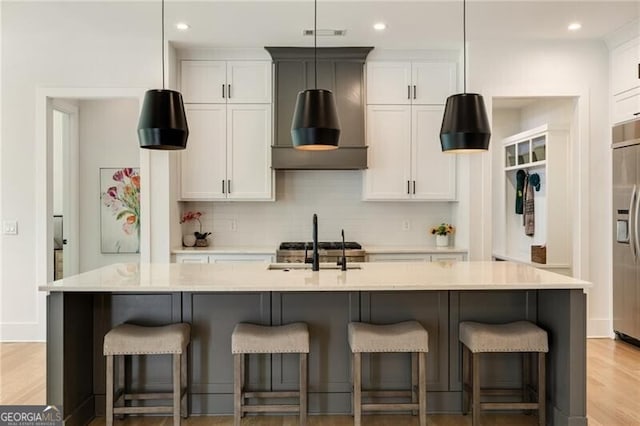 kitchen featuring an island with sink, white cabinetry, light countertops, backsplash, and built in refrigerator