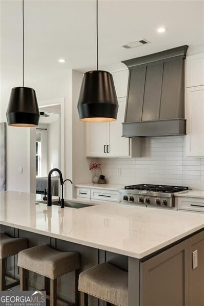 kitchen featuring a sink, decorative light fixtures, visible vents, backsplash, and custom range hood