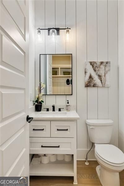 half bath with toilet, vanity, and wood finished floors