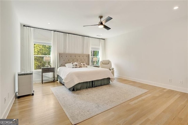 bedroom featuring radiator, multiple windows, light wood-style flooring, and baseboards