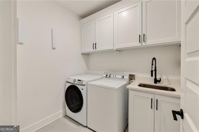 washroom featuring a sink, cabinet space, washing machine and clothes dryer, baseboards, and light tile patterned flooring