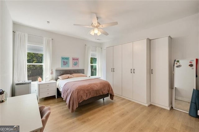 bedroom with a ceiling fan, multiple windows, light wood finished floors, and a closet