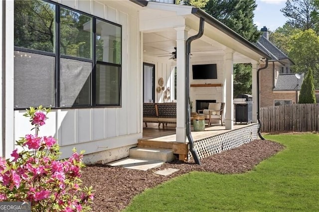 doorway to property with fence, a deck, board and batten siding, ceiling fan, and a yard