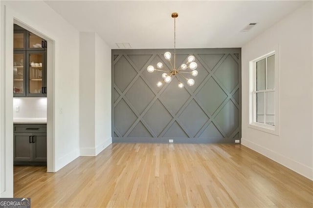 unfurnished dining area featuring baseboards, a decorative wall, a chandelier, and light wood-style flooring