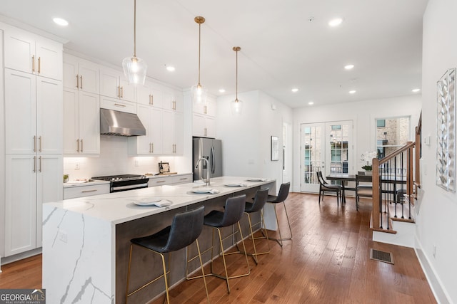 kitchen featuring a kitchen island with sink, dark wood finished floors, under cabinet range hood, stainless steel appliances, and white cabinetry