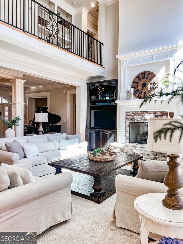 living area featuring ornamental molding, ornate columns, a stone fireplace, and a high ceiling