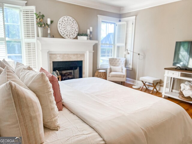 bedroom with baseboards, ornamental molding, a fireplace, and wood finished floors