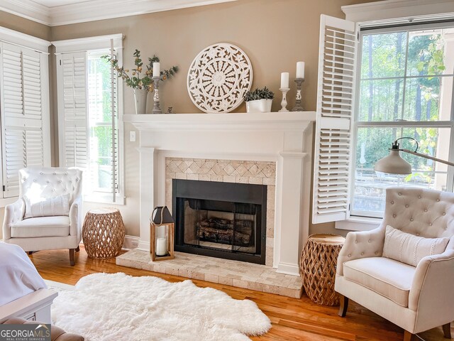 living area with a tiled fireplace, ornamental molding, wood finished floors, and a healthy amount of sunlight