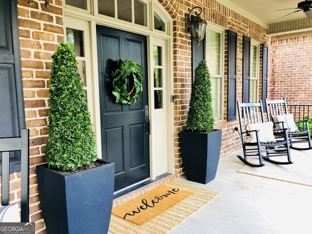 doorway to property featuring covered porch, ceiling fan, and brick siding