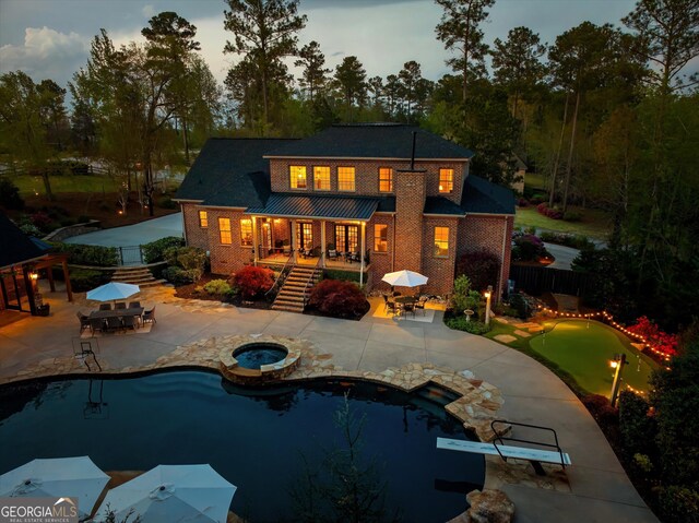 back of house featuring stairs, an in ground hot tub, a patio, and brick siding