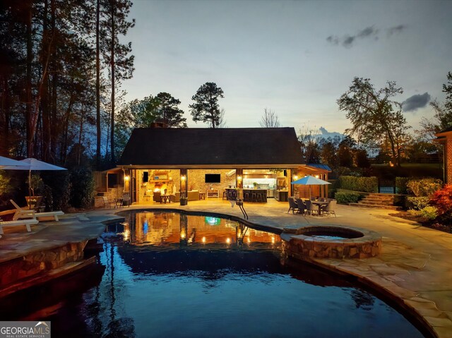pool at dusk with an outdoor structure, a pool with connected hot tub, an outdoor bar, a patio, and an exterior structure