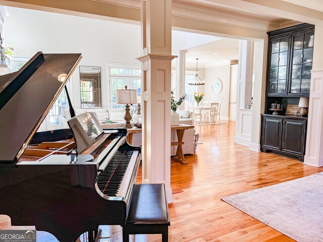 living area featuring crown molding, light wood finished floors, ornate columns, and an inviting chandelier