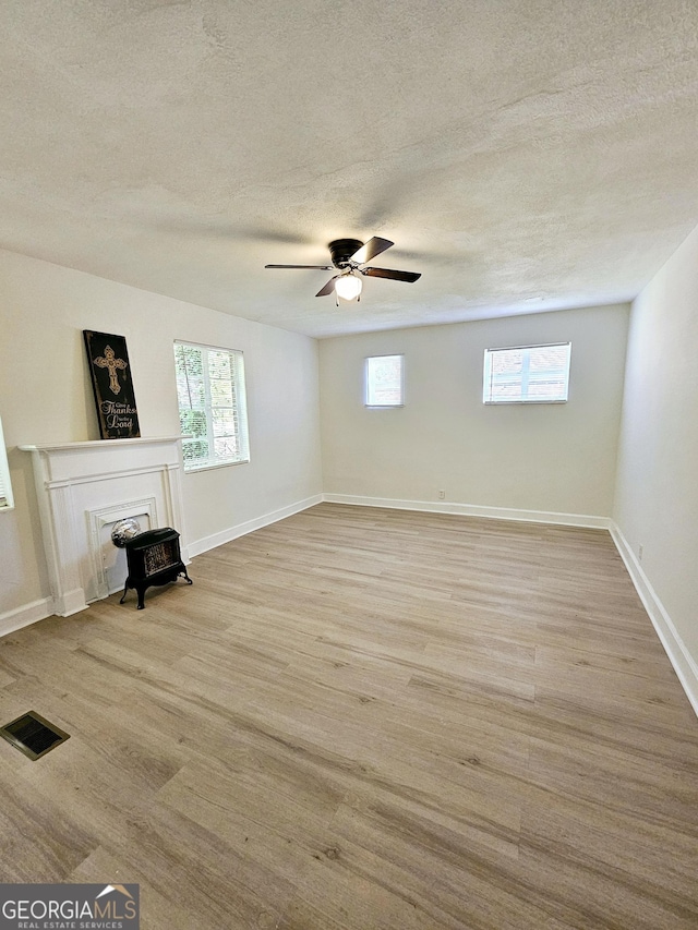 unfurnished living room featuring a textured ceiling, a healthy amount of sunlight, and a wood stove