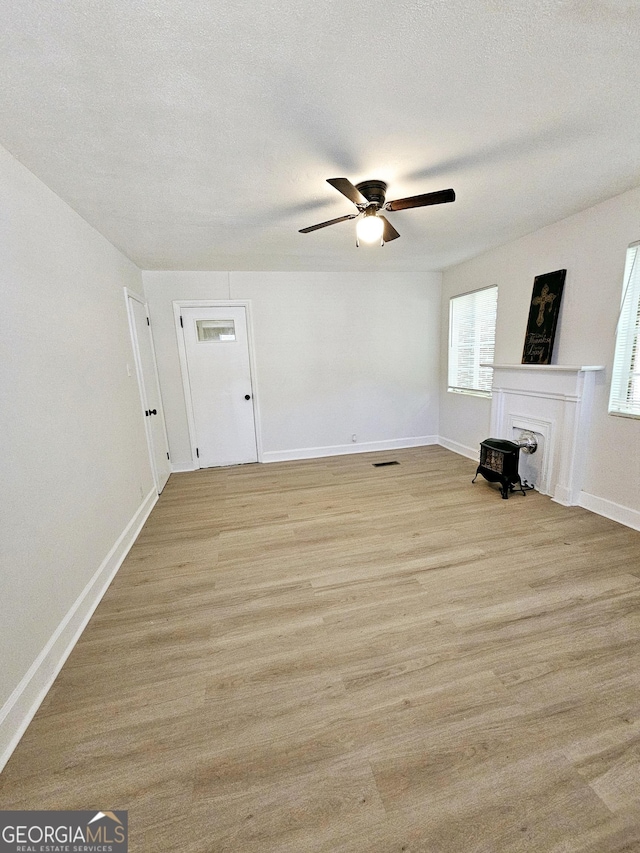 unfurnished living room with baseboards, a ceiling fan, light wood finished floors, and a wood stove