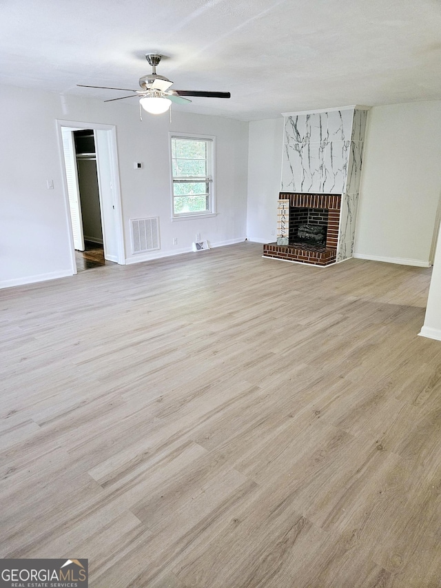 unfurnished living room featuring ceiling fan, a brick fireplace, baseboards, wood finished floors, and visible vents
