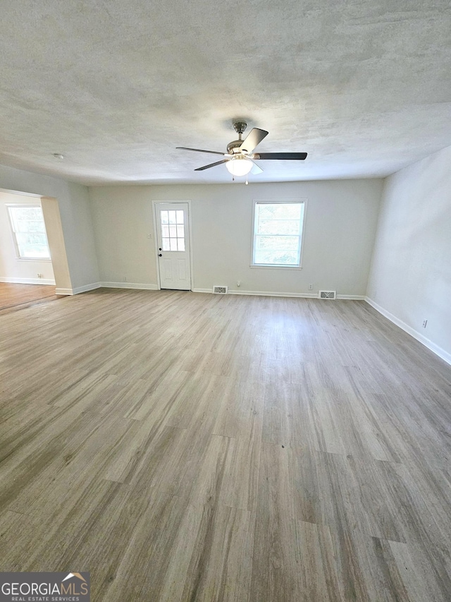 unfurnished living room featuring visible vents, a ceiling fan, baseboards, and wood finished floors