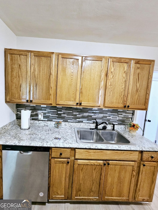 kitchen featuring stainless steel dishwasher, a sink, backsplash, and light stone countertops