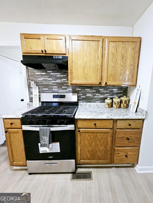 kitchen featuring visible vents, gas range, tasteful backsplash, light wood finished floors, and under cabinet range hood