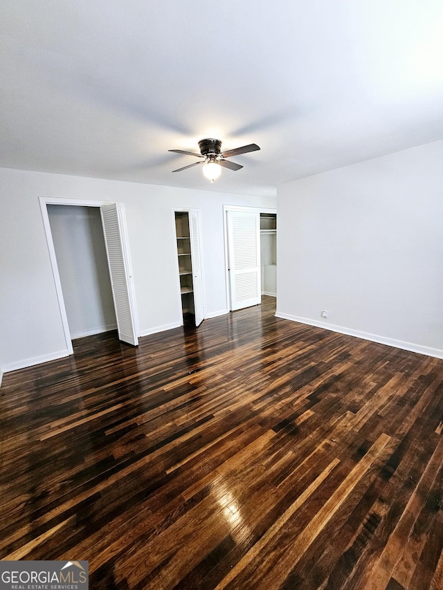 unfurnished bedroom with multiple closets, baseboards, dark wood-style flooring, and ceiling fan