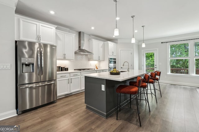 kitchen featuring a kitchen island with sink, wall chimney exhaust hood, white cabinetry, a sink, and stainless steel appliances