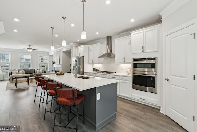 kitchen with wall chimney range hood, appliances with stainless steel finishes, a sink, a large island, and a kitchen bar
